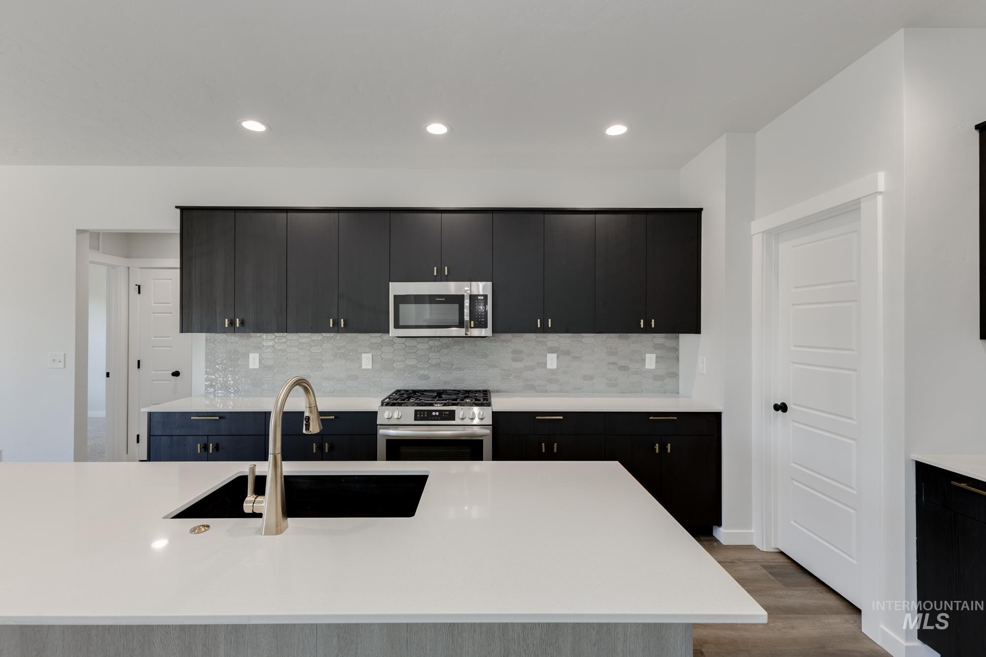Kitchen with stainless steel appliances, decorative backsplash, light stone countertops, dark cabinetry, and dark wood-style flooring