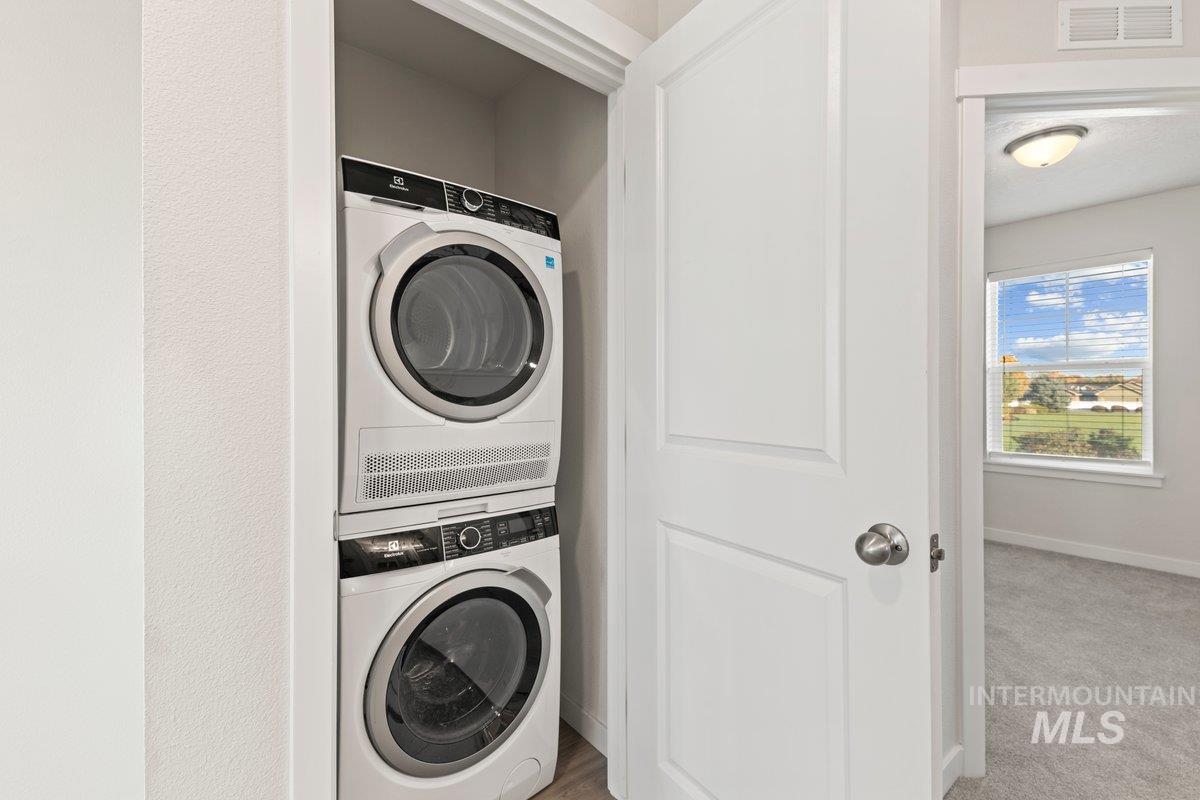 Laundry room with stacked washer / drying machine and carpet floors
