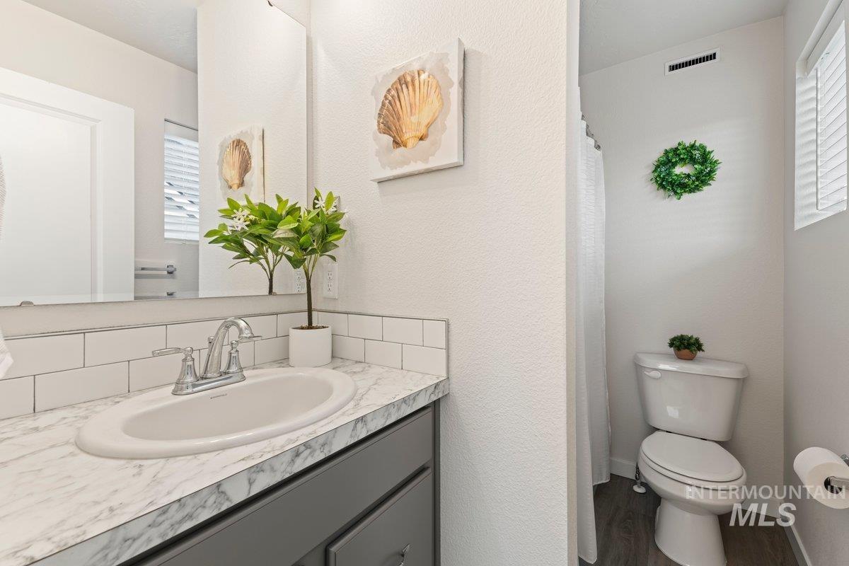 Full bath featuring vanity, a shower with curtain, dark wood-style floors, a textured wall, and tasteful backsplash