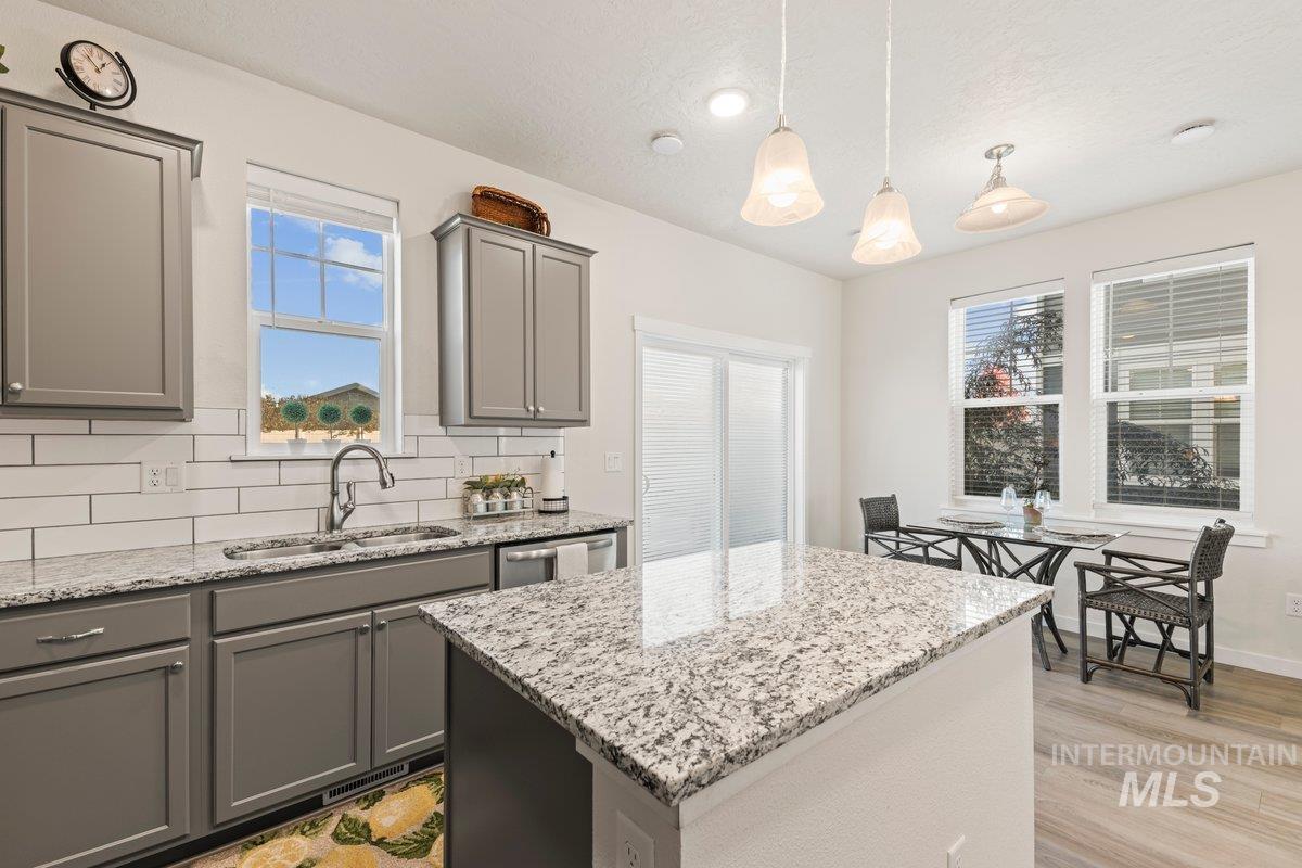 Kitchen featuring light stone countertops, tasteful backsplash, hanging light fixtures, and gray cabinets