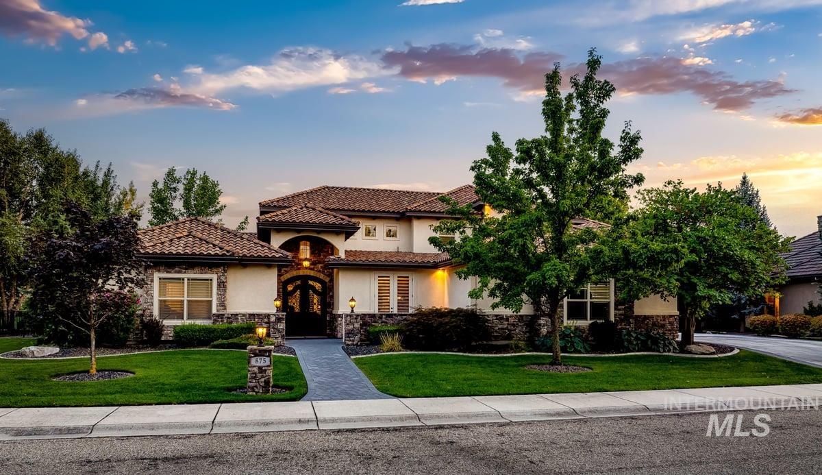 Mediterranean / spanish home featuring stone siding, a lawn, a tiled roof, and stucco siding