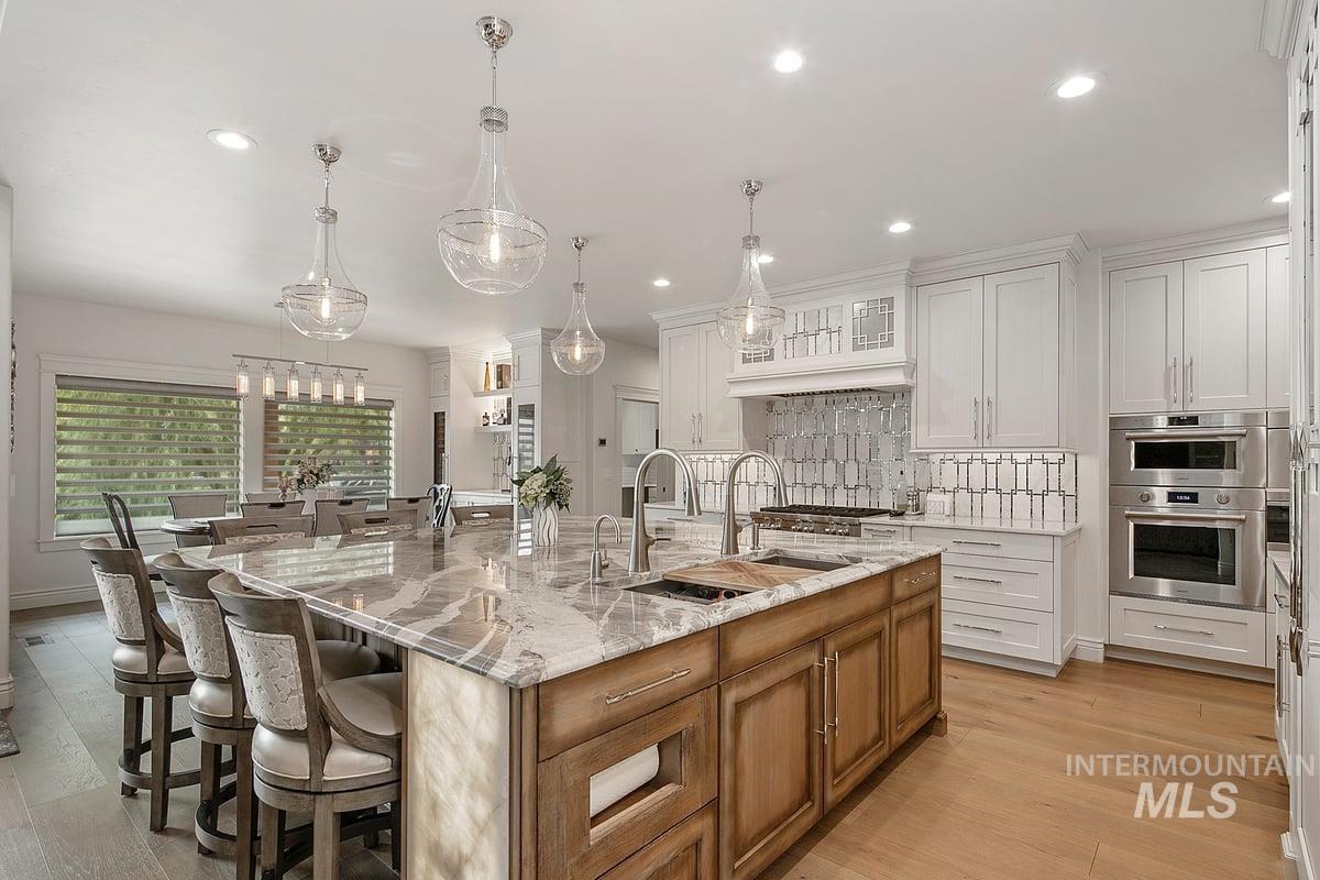 Kitchen featuring brown cabinetry, a breakfast bar, a large island with sink, decorative backsplash, and white cabinetry