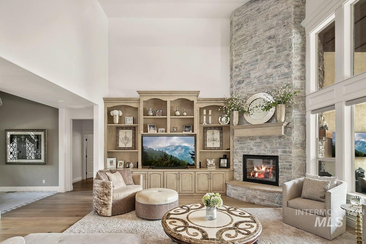 Living room featuring light wood-type flooring, a towering ceiling, and a stone fireplace