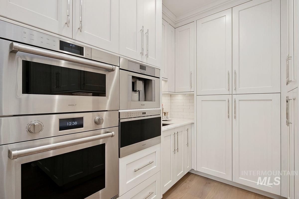Kitchen featuring stainless steel double oven, tasteful backsplash, white cabinets, and light wood-style flooring