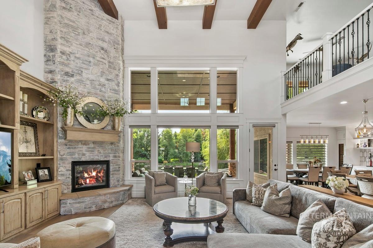 Living room with a stone fireplace, beam ceiling, a high ceiling, and healthy amount of natural light