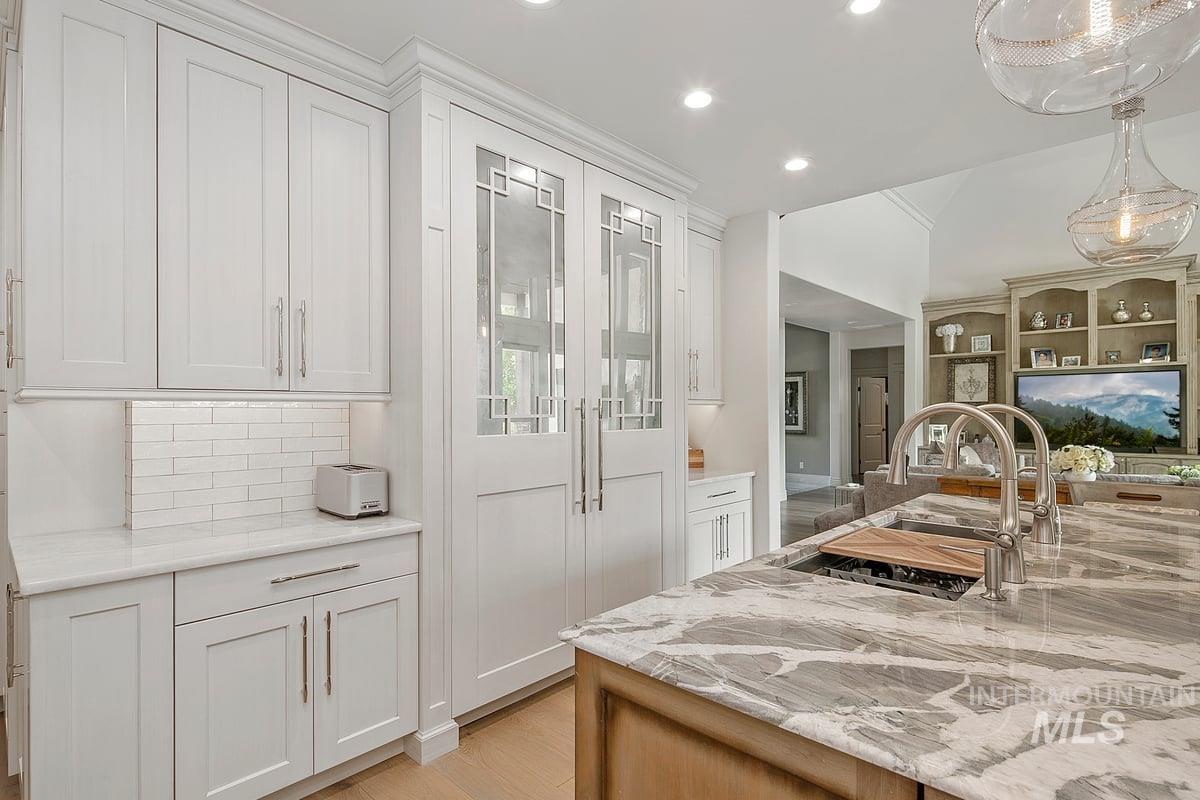 Kitchen featuring white cabinets, light stone counters, hanging light fixtures, recessed lighting, and light wood-type flooring
