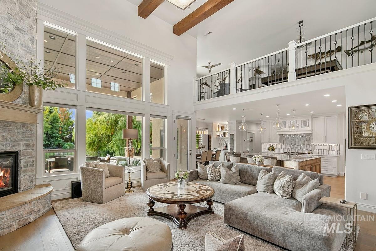 Living room with hardwood / wood-style flooring, a stone fireplace, ceiling fan, a high ceiling, and beamed ceiling