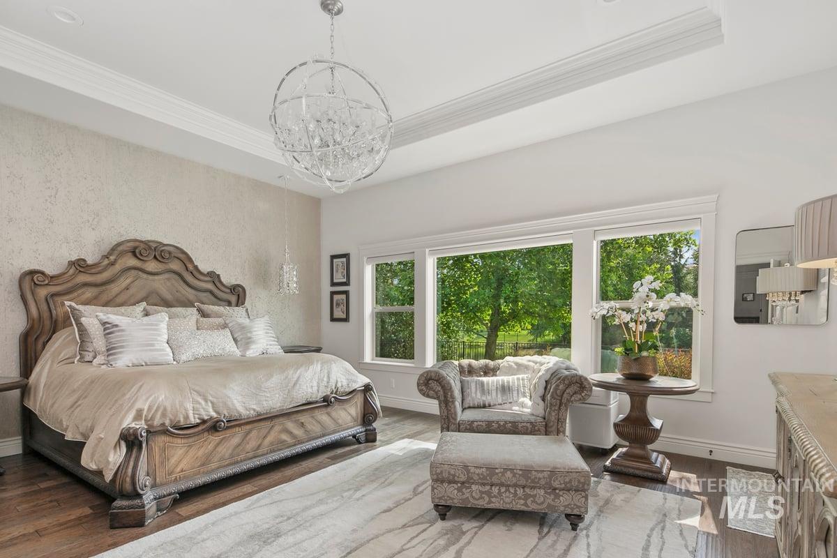 Bedroom featuring wood finished floors, a raised ceiling, multiple windows, crown molding, and a chandelier
