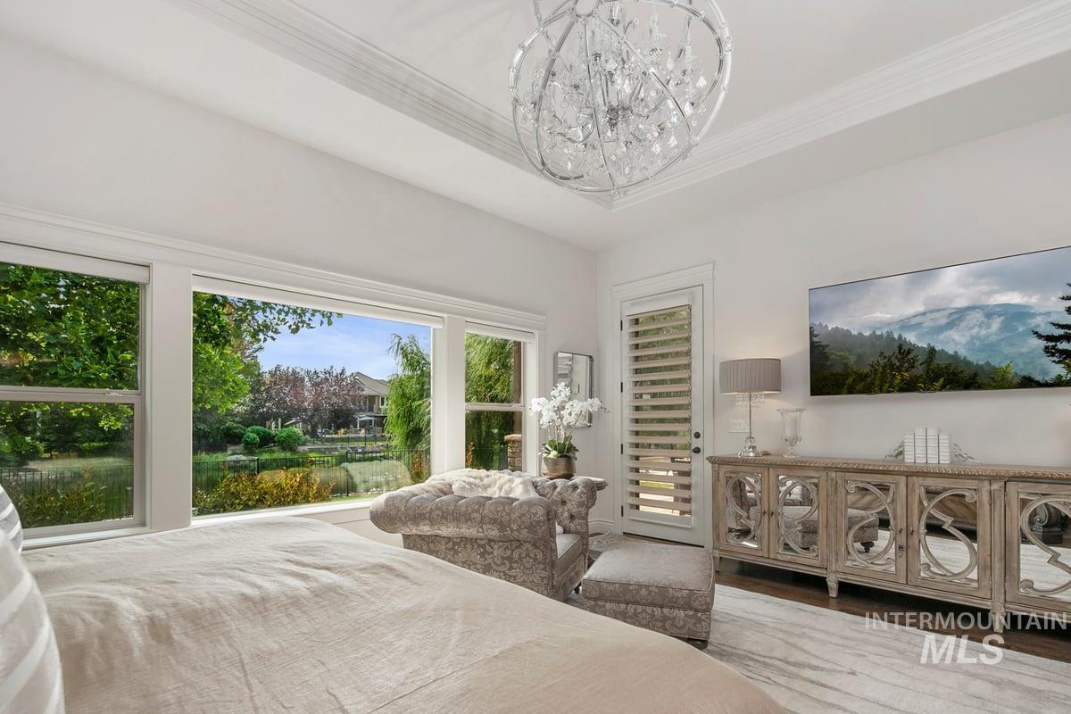Bedroom featuring wood finished floors, ornamental molding, a chandelier, and a raised ceiling