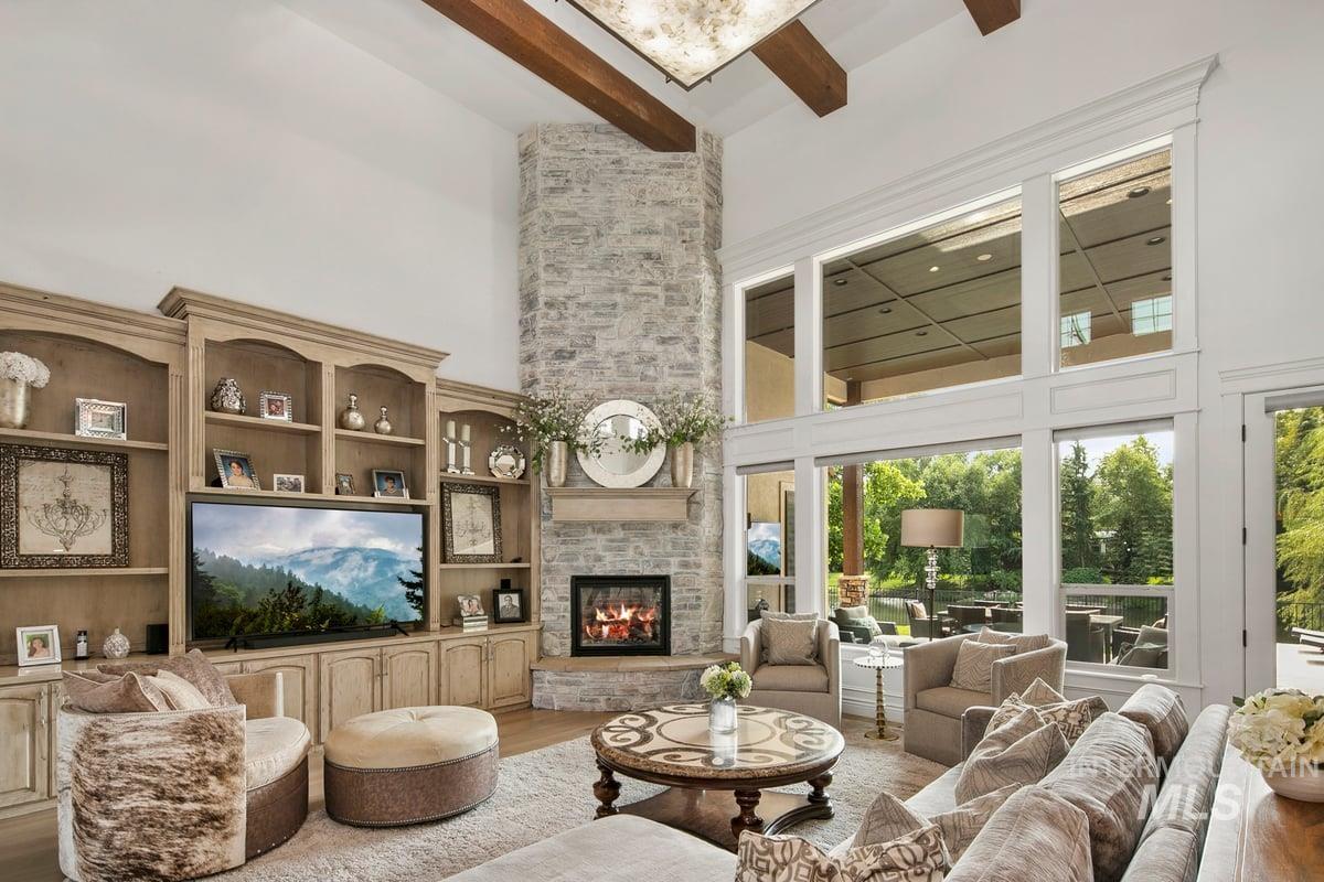 Living room featuring a stone fireplace, beamed ceiling, wood finished floors, a high ceiling, and built in features