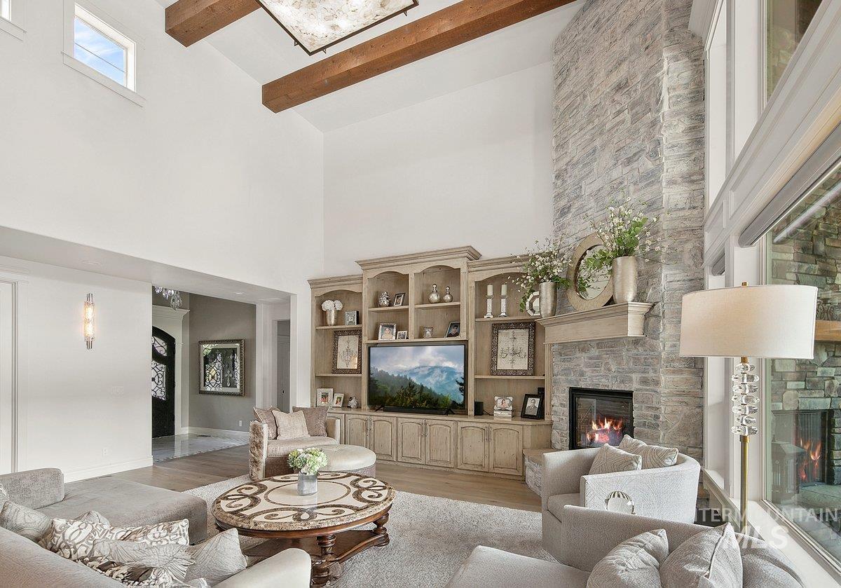 Living area with a fireplace, beamed ceiling, light wood-style floors, and a high ceiling