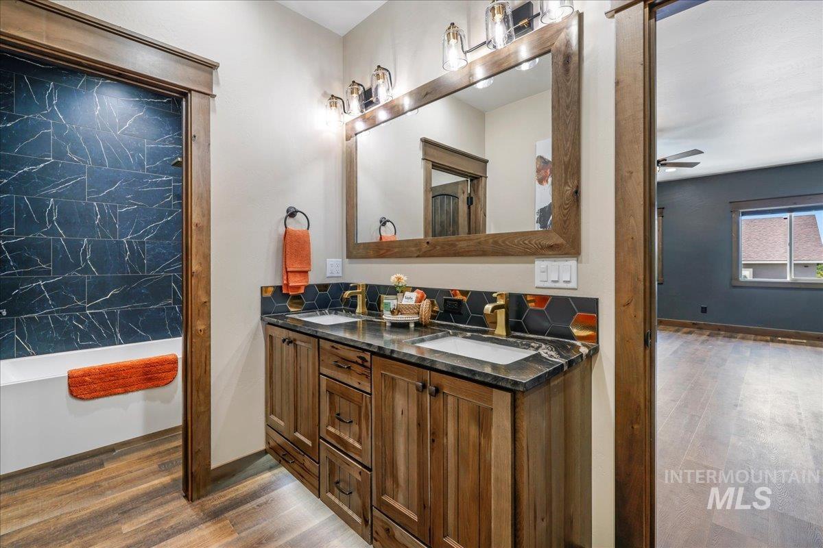 Full bath with dark wood-style floors, double vanity, a ceiling fan, and a soaking tub