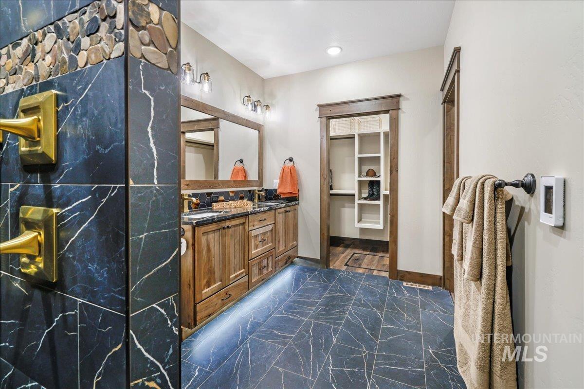 Bathroom with double vanity, dark marble finish flooring, and a spacious closet