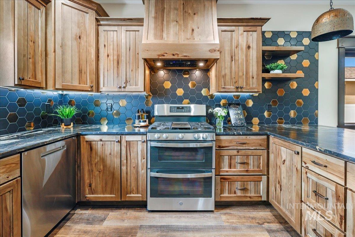 Kitchen featuring dark stone counters, appliances with stainless steel finishes, custom range hood, decorative backsplash, and open shelves