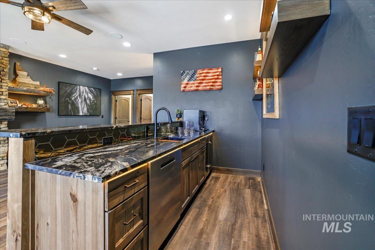 Kitchen featuring dark wood-style flooring, dishwasher, a peninsula, a ceiling fan, and dark stone counters