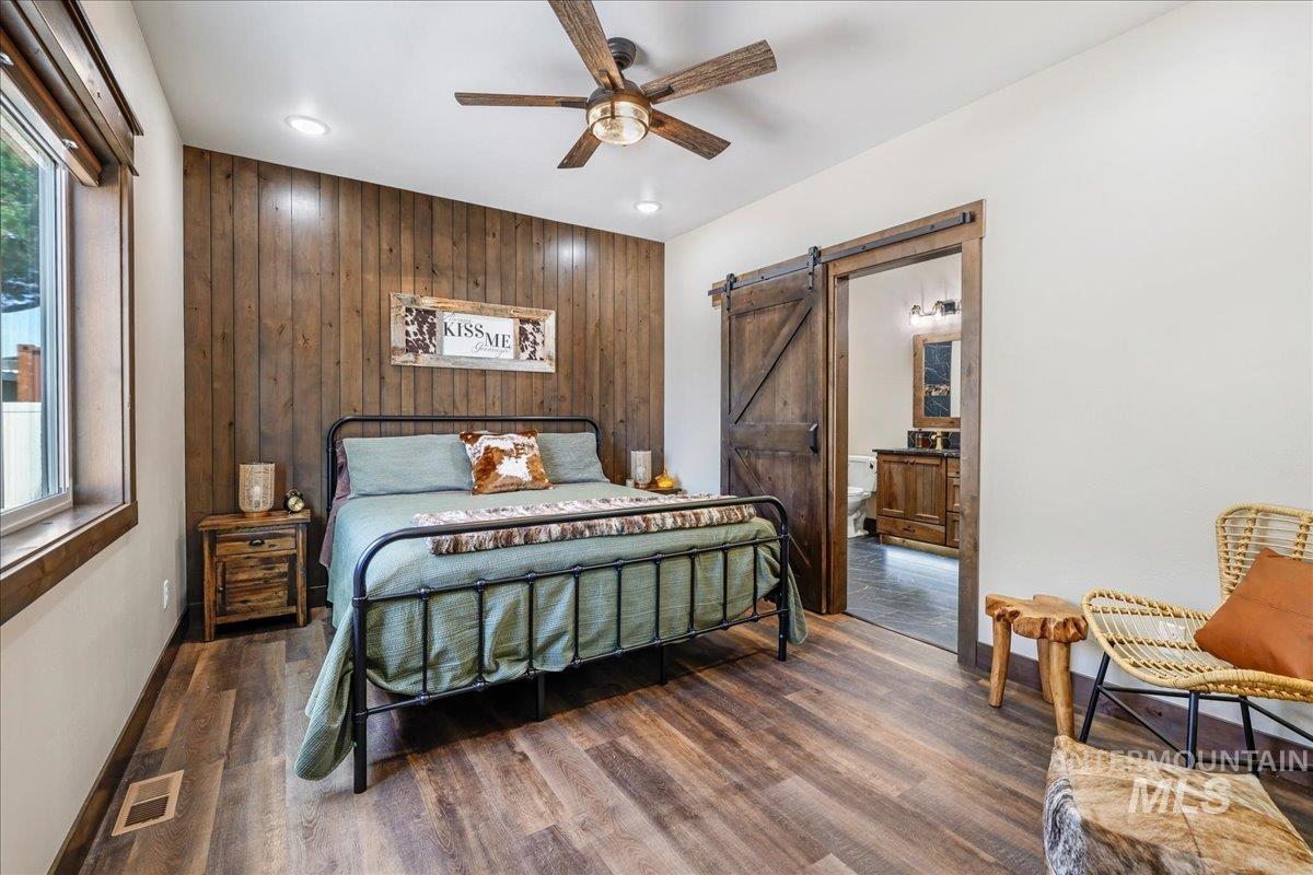 Bedroom with wood walls, a barn door, dark wood finished floors, and ceiling fan