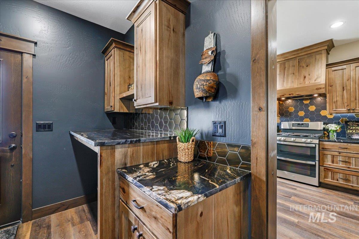 Kitchen with tasteful backsplash, dark wood-style floors, range with two ovens, a textured wall, and brown cabinetry