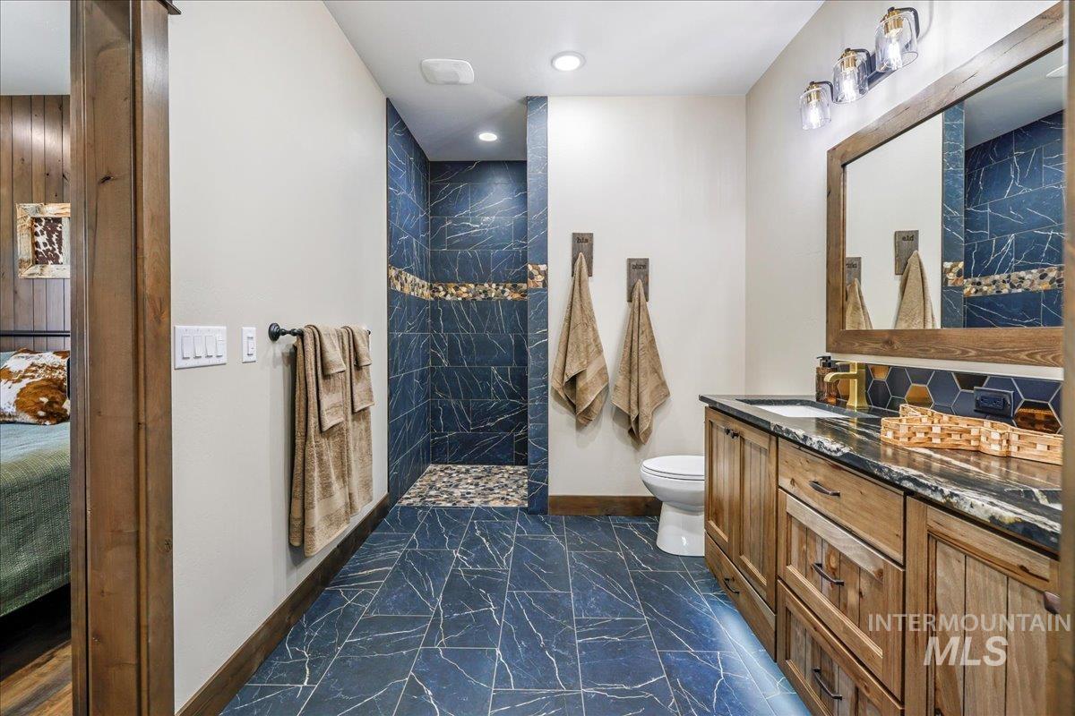 Full bath with vanity, walk in shower, dark marble finish floors, recessed lighting, and decorative backsplash