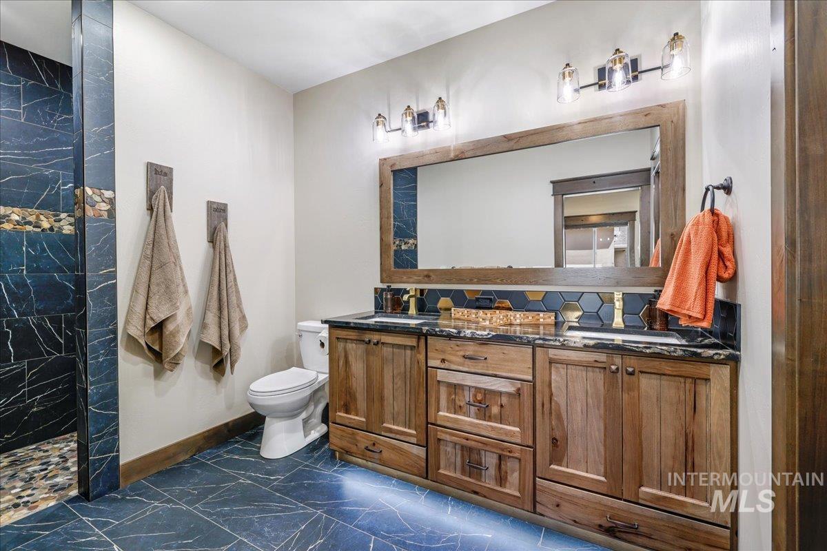 Full bathroom featuring double vanity, a walk in shower, and dark marble finish flooring
