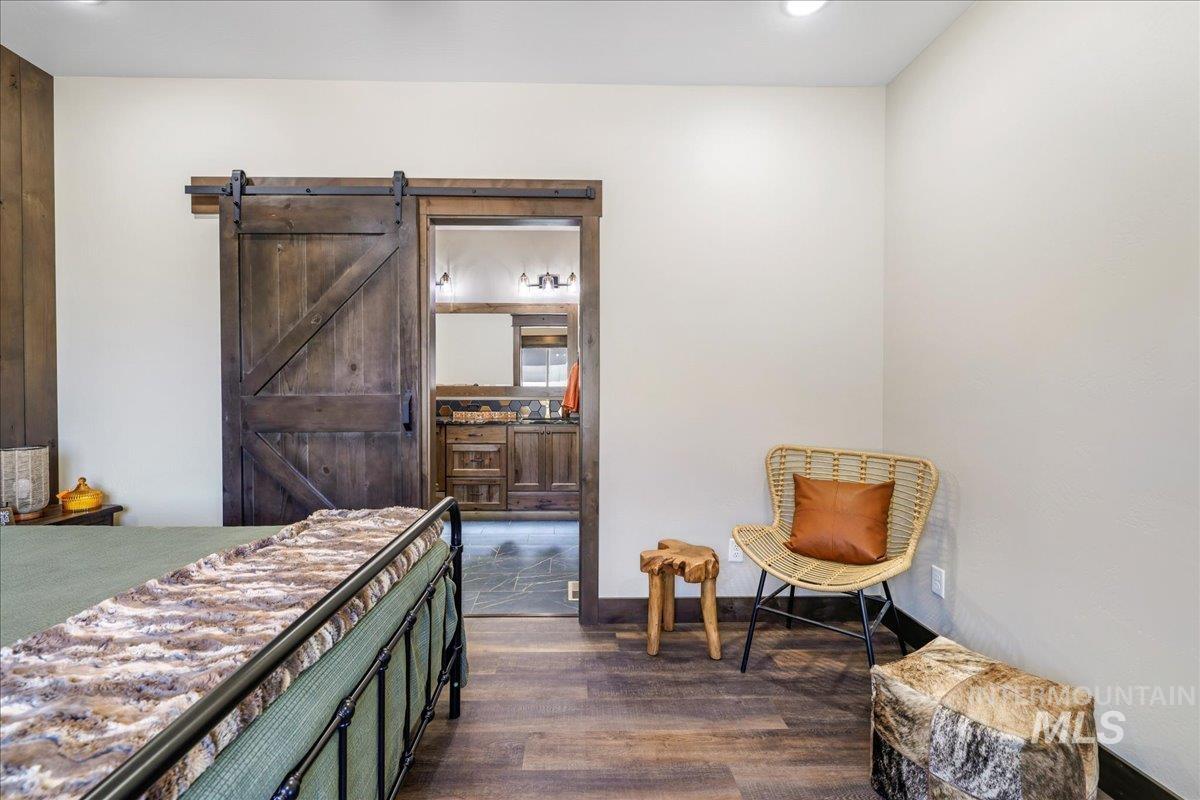 Bedroom featuring a barn door, dark wood-type flooring, and connected bathroom
