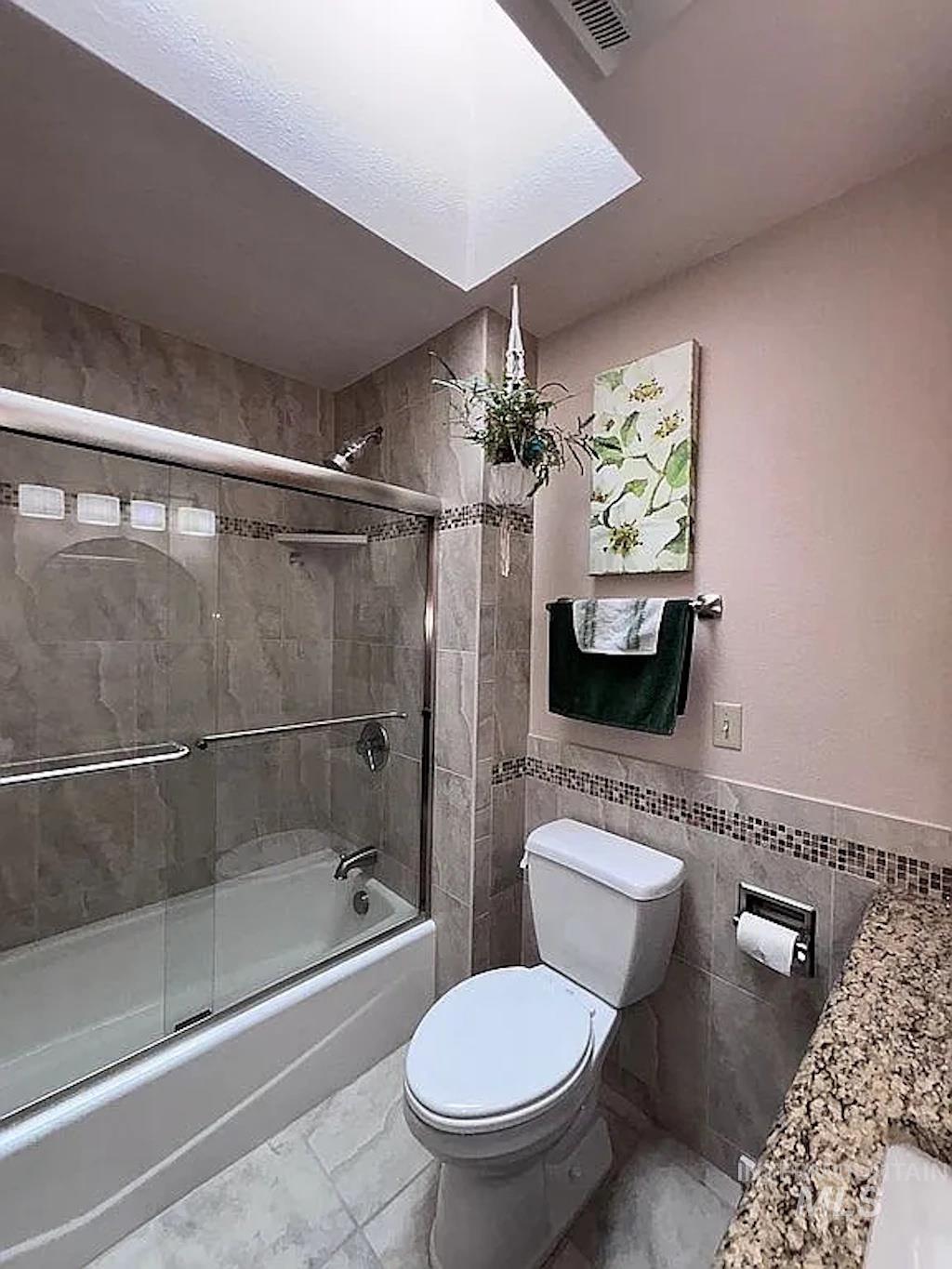 Bathroom featuring a skylight, tile flooring, a bathtub with sliding glass doors, and a tiled shower surround