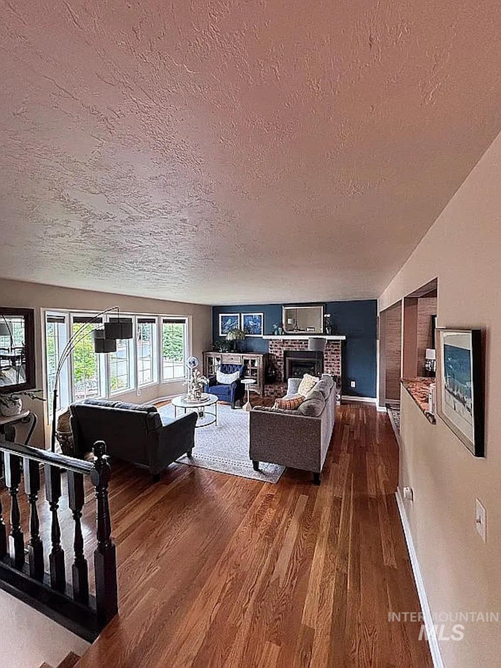 Hardwood flooring extends throughout this expansive living space, featuring a brick fireplace with a dark accent wall