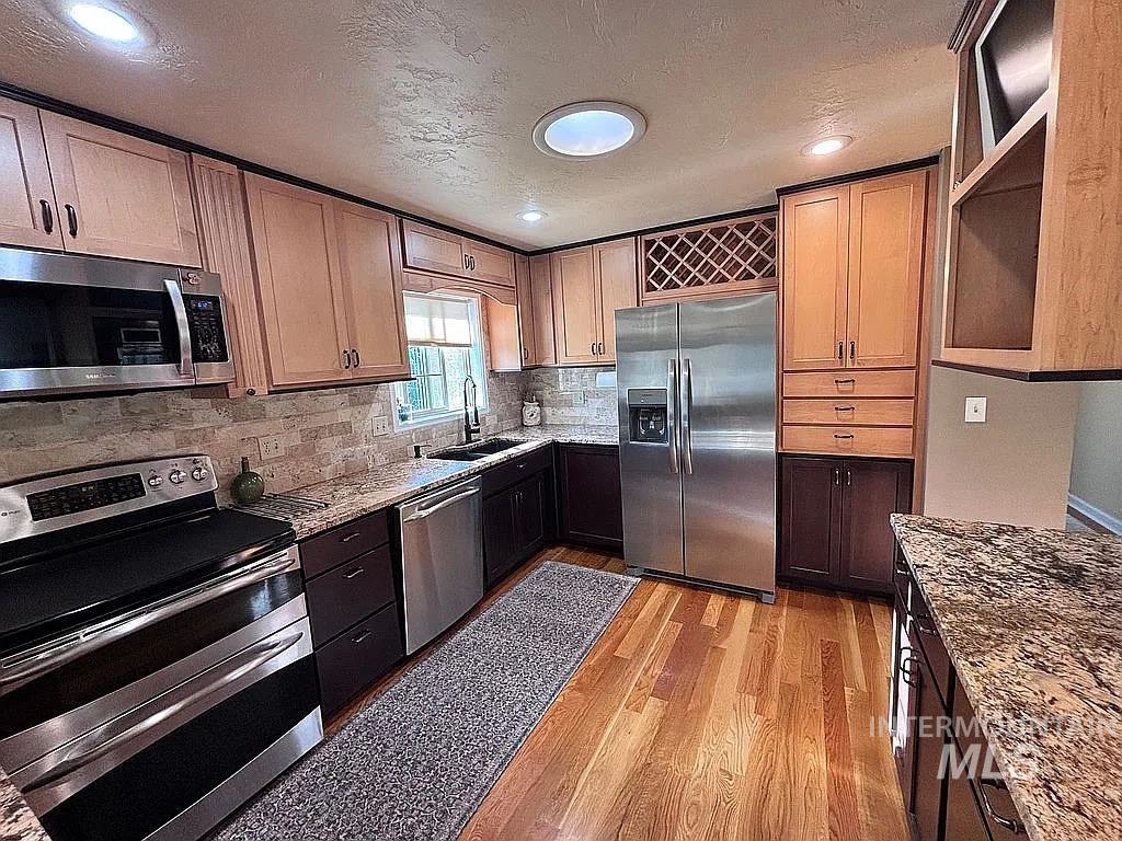 Kitchen featuring light wood upper cabinetry and dark wood lower cabinetry, stainless steel appliances, granite countertops, and wood-finish flooring