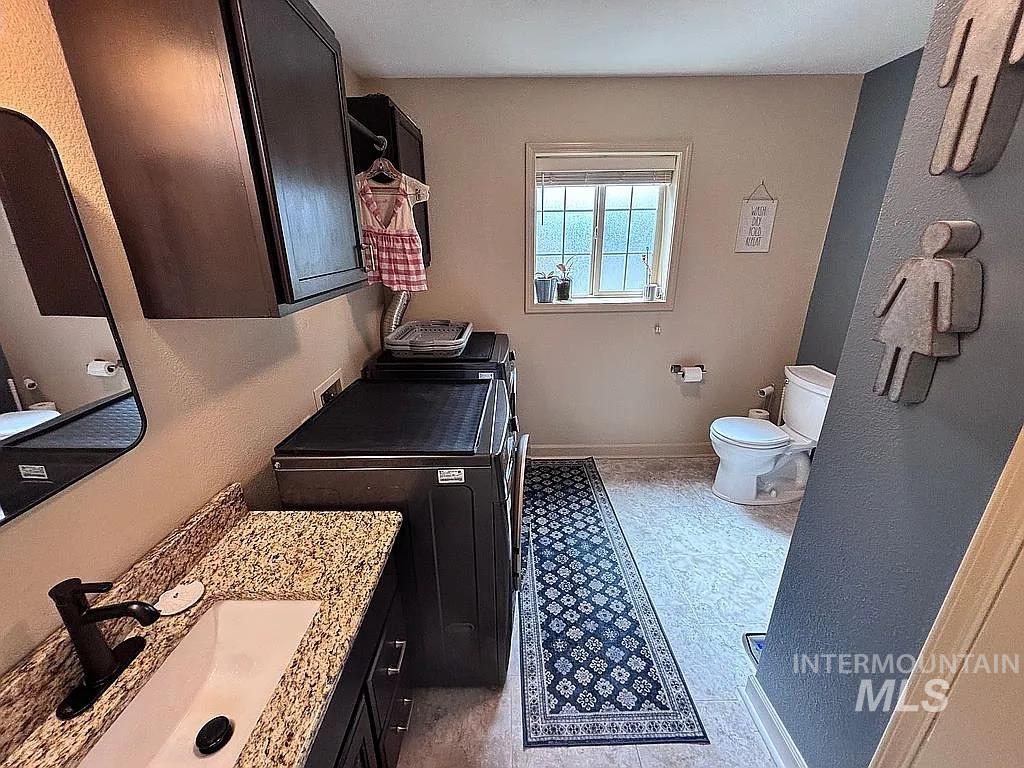 Combined laundry and bath area featuring a white rectangular sink, a granite-finish countertop, and dark wood-finish cabinetry