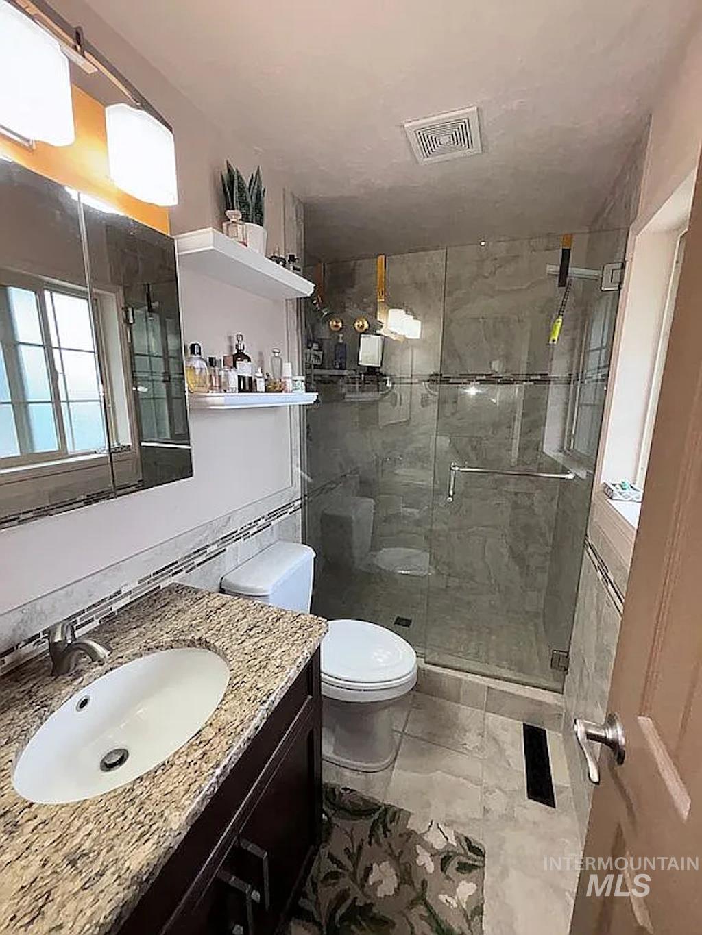 Bathroom featuring a dark wood-finish vanity with a granite countertop and undermount sink, a framed mirror, and a glass-enclosed shower with tile surround