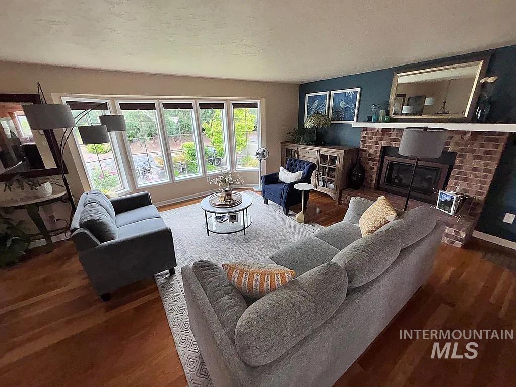 Spacious living area featuring wood-finish flooring, a brick fireplace with hearth, and a large bay window with multiple panes