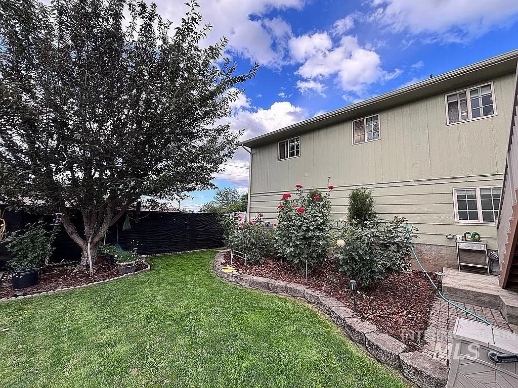 Expansive backyard featuring a manicured lawn, established shade tree, and well-maintained garden beds with blooming shrubs