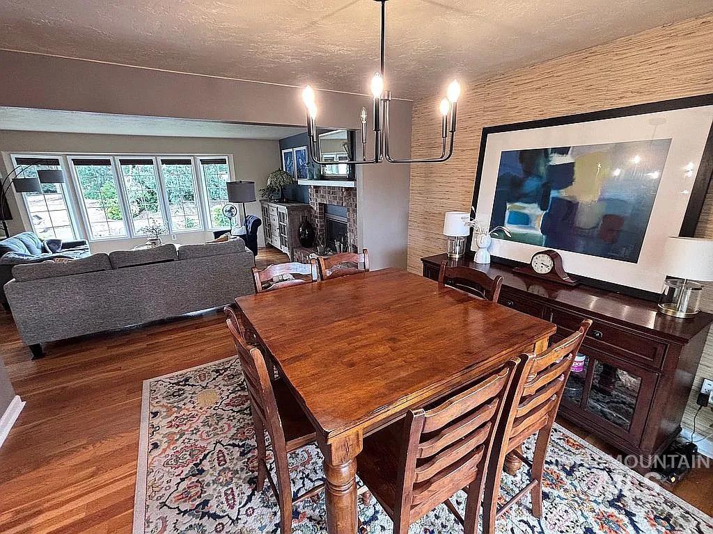 Dining area featuring wood-finish flooring, a contemporary chandelier, and textured wall covering