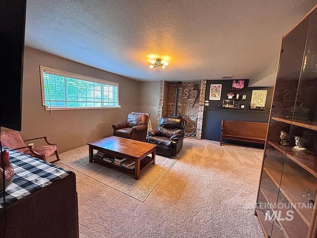 Carpeted room featuring a horizontal window with blinds, a brick accent wall, a visible stove pipe, and a ceiling-mounted light fixture
