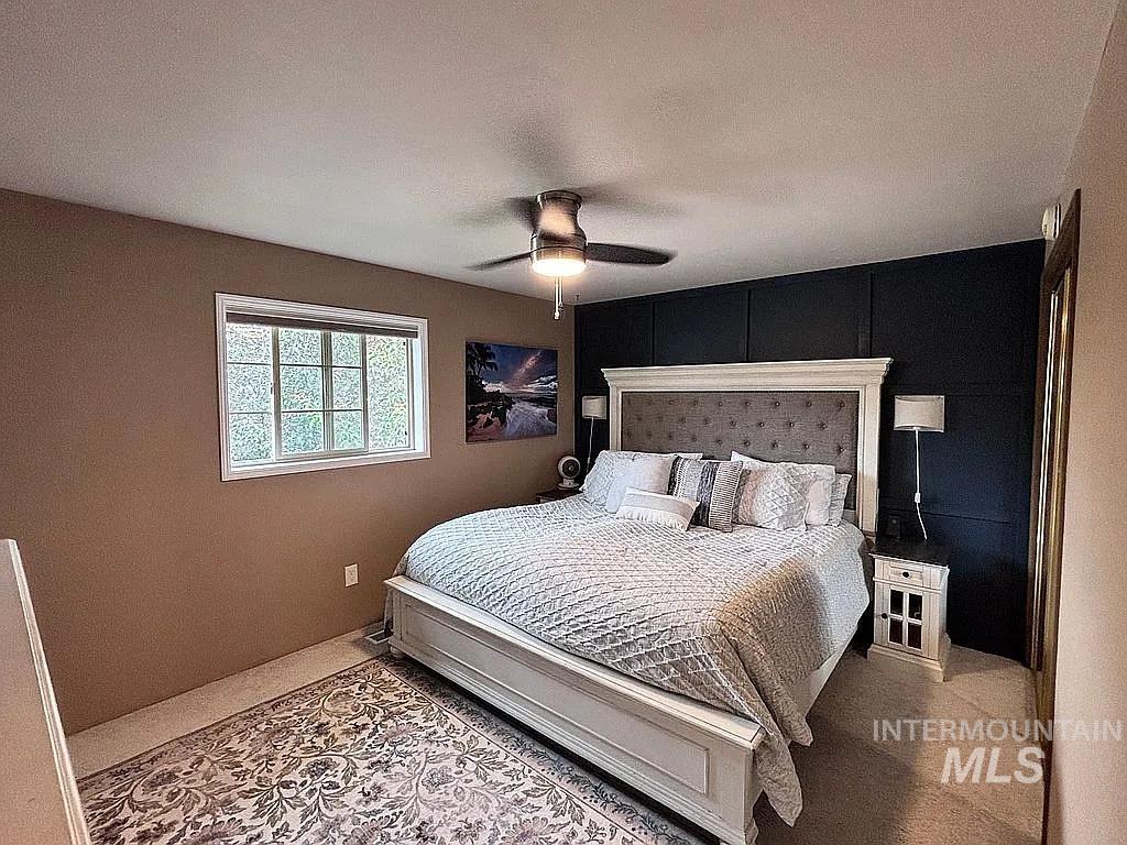 Bedroom featuring a ceiling fan, a window with a white frame, and a dark accent wall with paneling detail