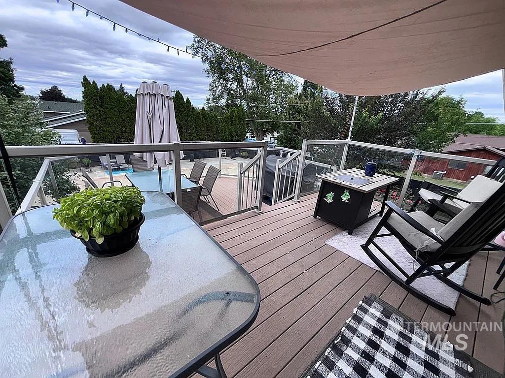 Multi-level composite deck featuring glass panel railings, a sun shade canopy, and stairs descending to a lower patio with an in-ground pool