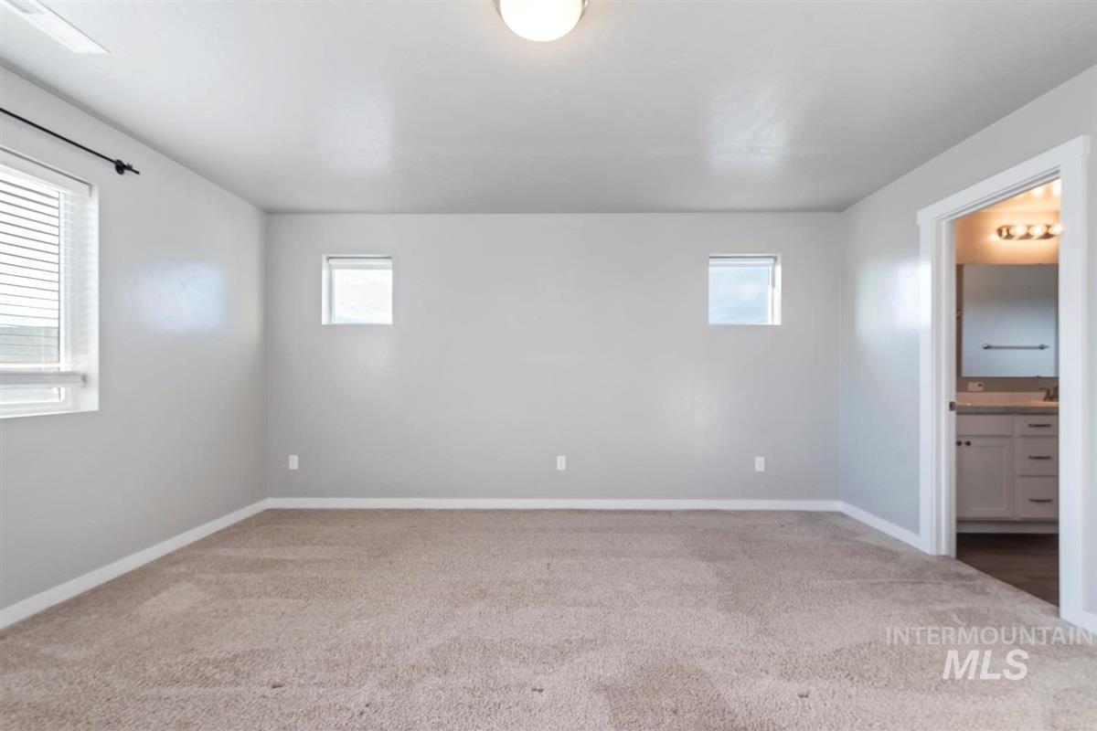 Unfurnished bedroom featuring light colored carpet, multiple windows, and ensuite bathroom