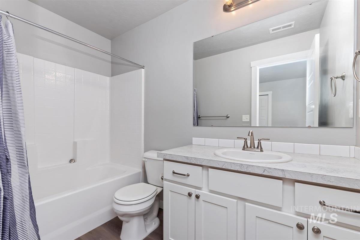 Full bath featuring vanity, shower / bath combo with shower curtain, and dark wood-style flooring