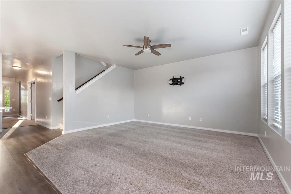 Unfurnished living room featuring ceiling fan, stairs, and dark carpet