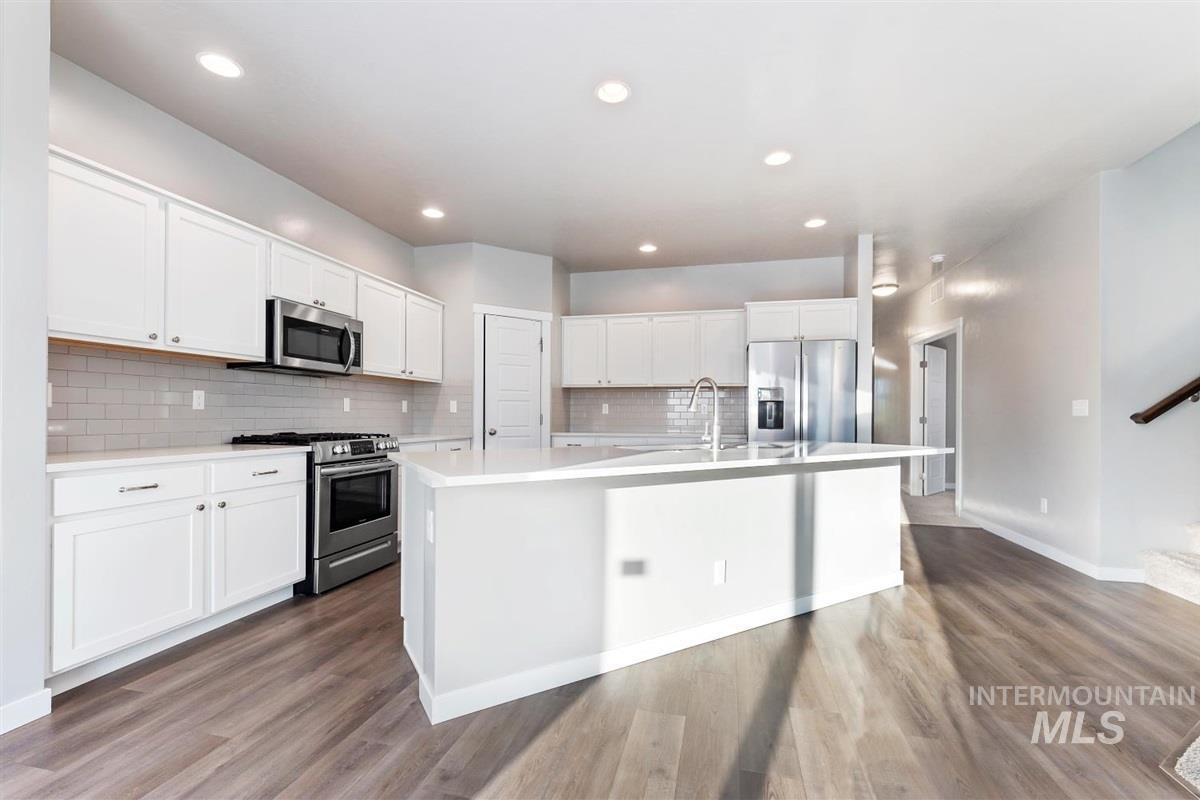Kitchen featuring appliances with stainless steel finishes, white cabinets, a center island with sink, tasteful backsplash, and recessed lighting