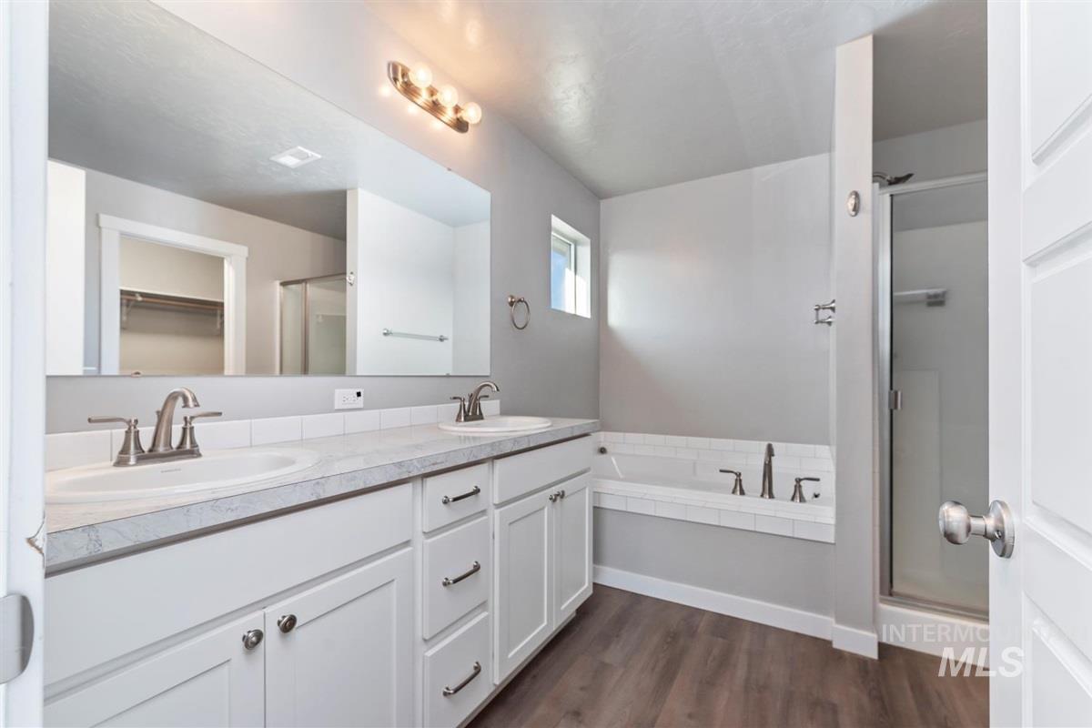 Full bathroom featuring a stall shower, double vanity, dark wood finished floors, and a bath