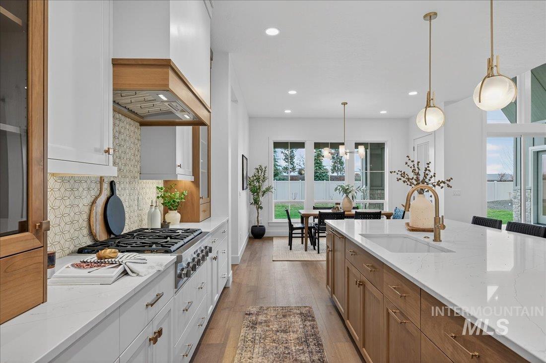 Kitchen featuring white cabinets, light stone countertops, hanging light fixtures, brown cabinetry, and recessed lighting