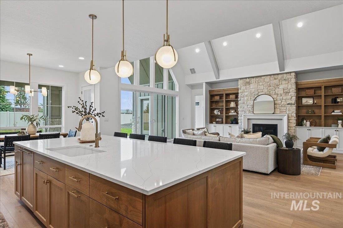 Kitchen with brown cabinetry, decorative light fixtures, a stone fireplace, a chandelier, and light wood finished floors
