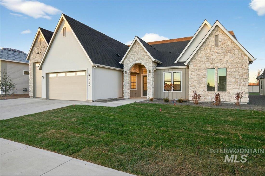 View of front of house with a front yard, stone siding, driveway, an attached garage, and stucco siding