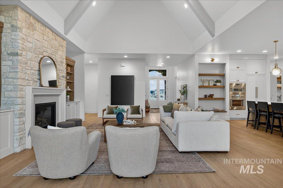 Living area with built in shelves, high vaulted ceiling, light wood-style floors, and a fireplace