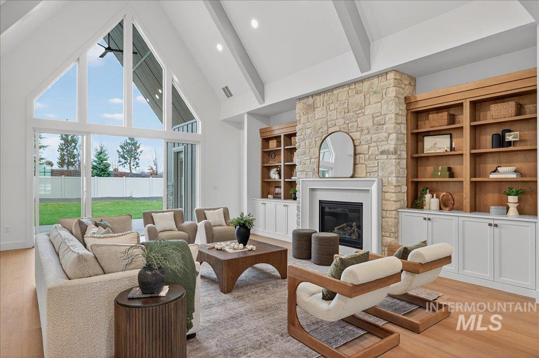 Living room featuring high vaulted ceiling, a large fireplace, light wood-style floors, beamed ceiling, and built in shelves