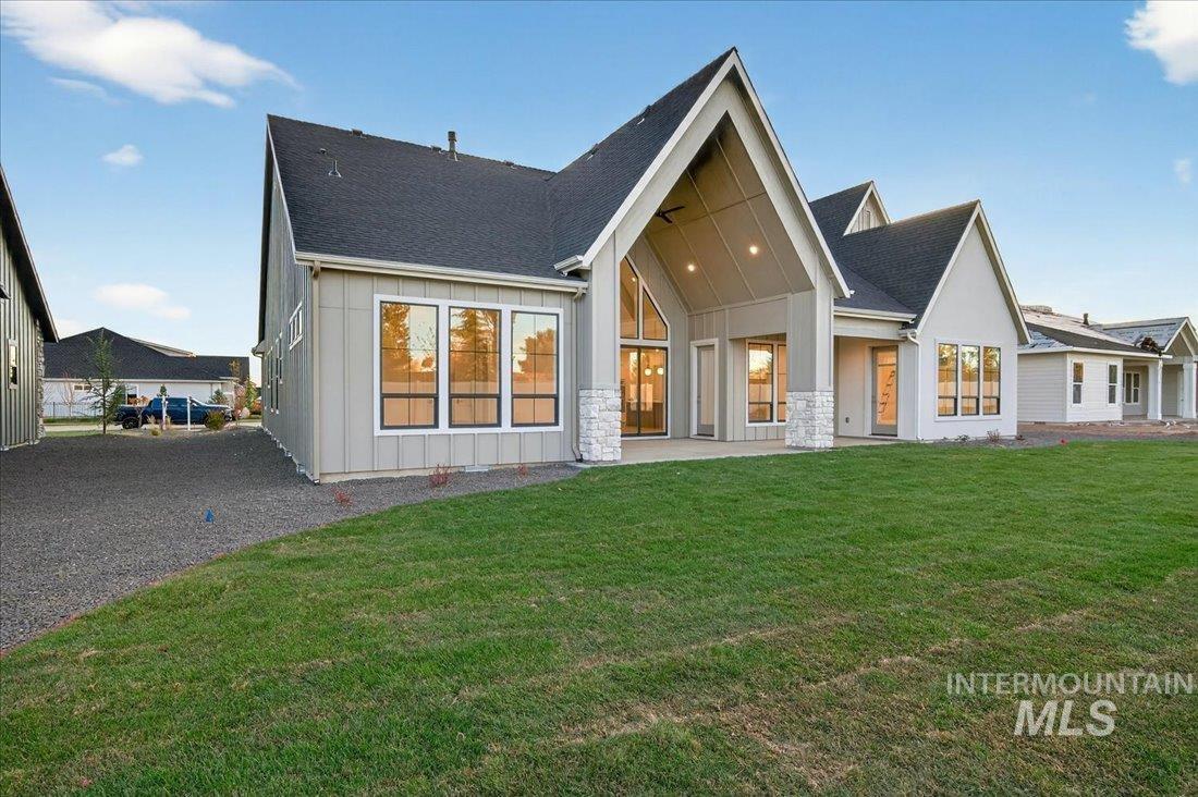 Rear view of property with a patio area, board and batten siding, roof with shingles, and a yard