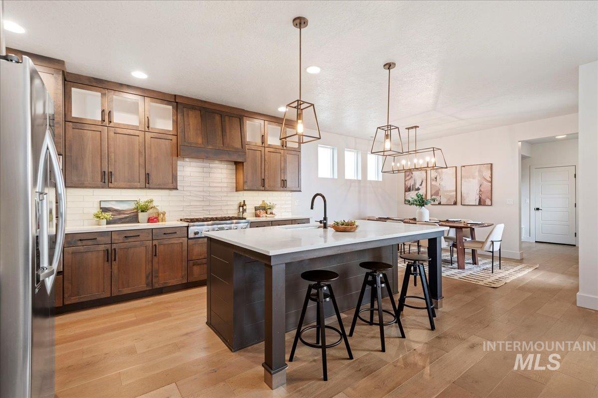 Kitchen featuring backsplash, stainless steel appliances, a kitchen bar, pendant lighting, and an island with sink