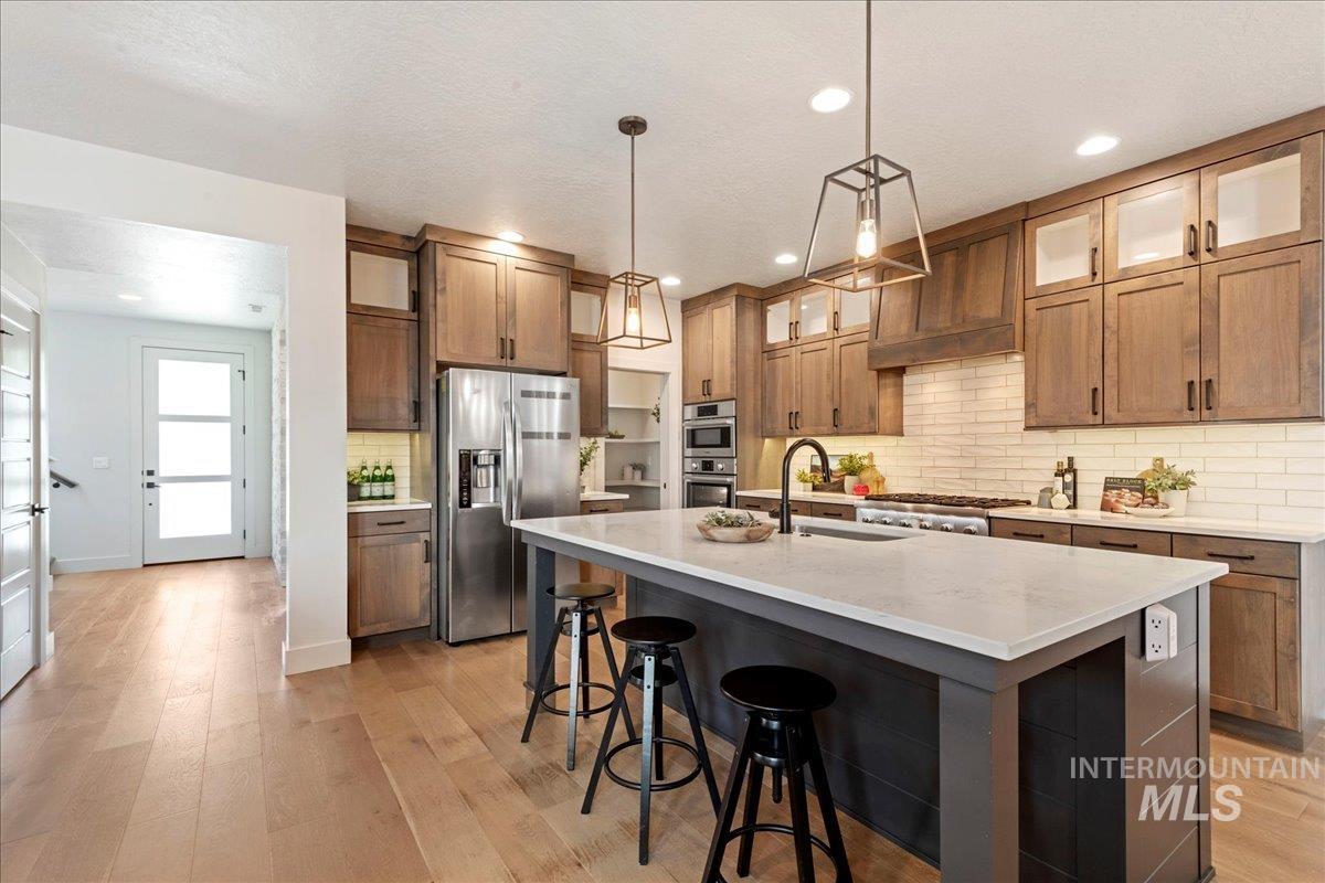 Kitchen with tasteful backsplash, stainless steel fridge, brown cabinets, light wood finished floors, and hanging light fixtures