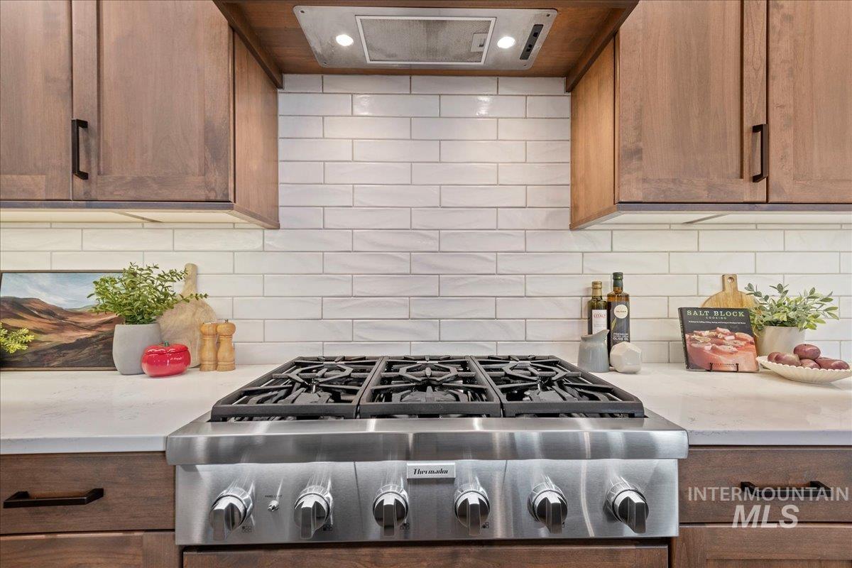 Kitchen view of decorative backsplash, stainless steel gas stovetop, extractor fan, and light stone counters