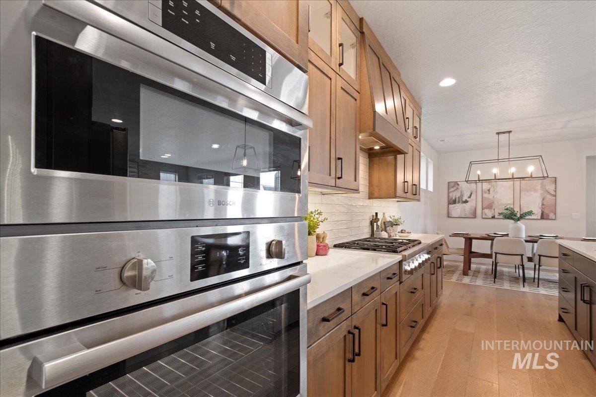 Kitchen featuring appliances with stainless steel finishes, hanging light fixtures, light wood-style floors, brown cabinets, and backsplash